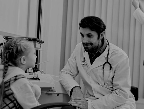 Male doctor talking with child patient while his colleague working in the background