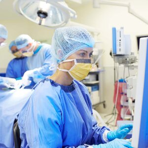 nurse in scrubs looking at a monitor in an operating room