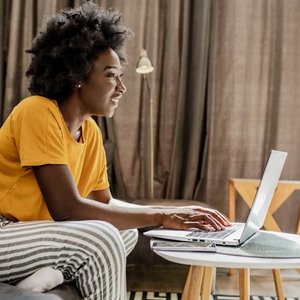 black woman in yellow shirt using laptop in bright room