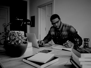 African american man in a home office using laptop and taking notes.
