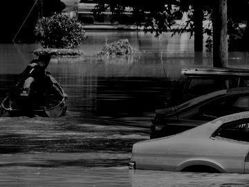 small motor boat going down a flooded street next to parked cars