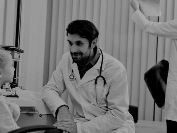 Male doctor talking with child patient while his colleague working in the background