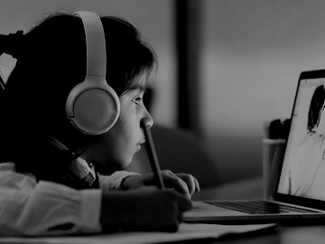 young girl wearing headphones watching a laptop where her teacher is writing on the white board