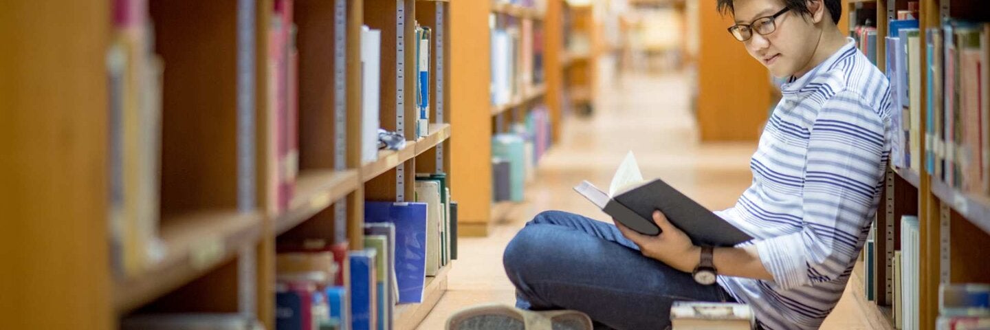 Young Asian man university student reading book in library