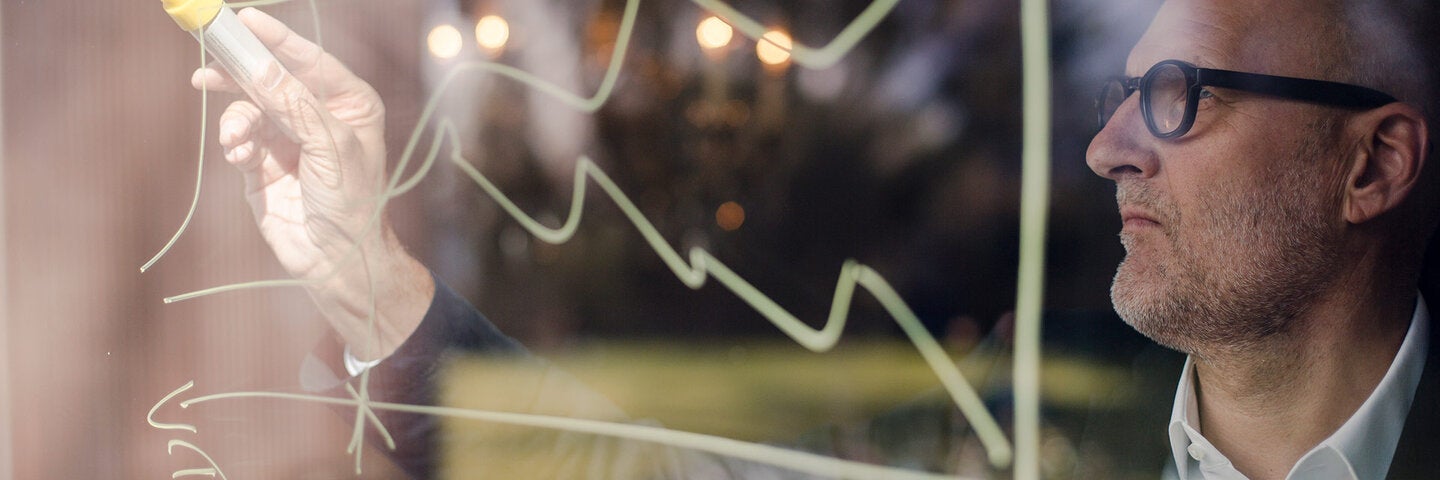 man with glasses writing a calculation on glass