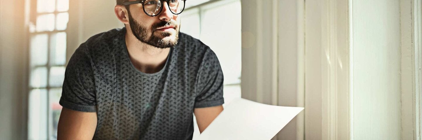 man in glasses writing while holding a paper in his other hand