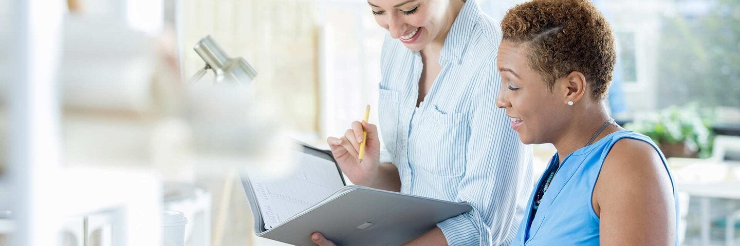 Confident female architects plan a project together. They are looking in a portfolio or calendar as they discuss the details of the project.