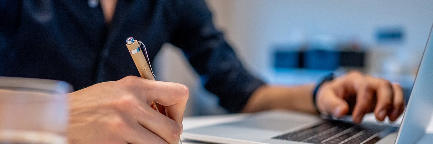 man writing and using a laptop