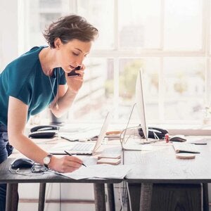 woman standing, talking on phone, taking notes over a table
